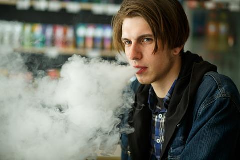 Teenage vaper blowing vapour by vape display